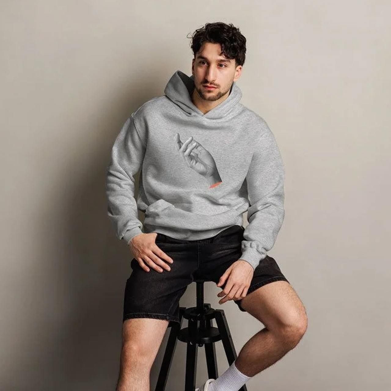 A man in a gray hoodie with a chest print of a statue’s hand.